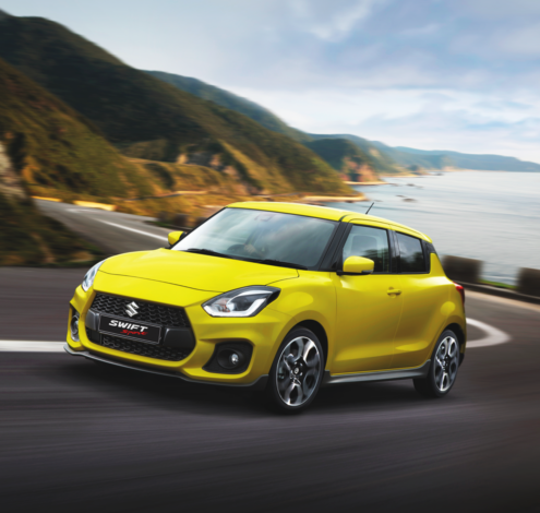 Yellow Swift Sport driving alongside an ocean view