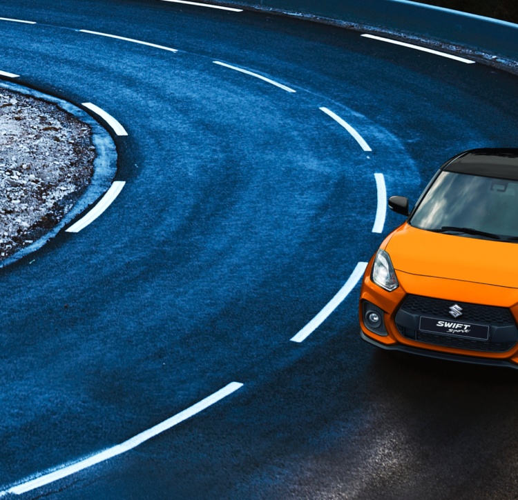 Orange two-tone Swift Sport driving on snowy mountain road